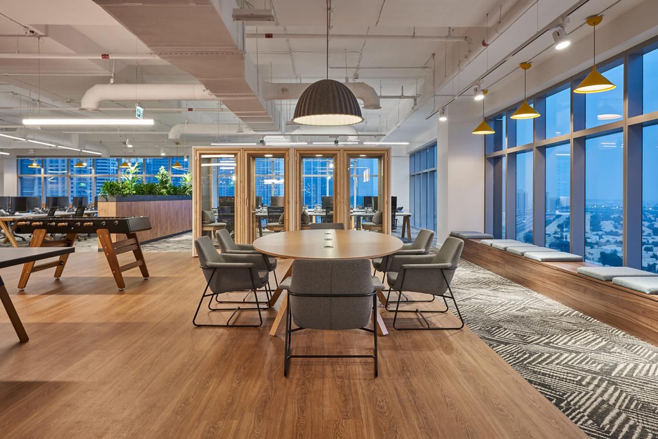 Open office meeting area with a round table beside floor to ceiling glazing and timber-framed glass rooms