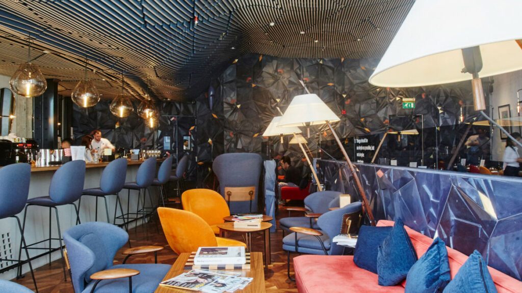 Lounge with blue and mustard armchairs, a pink banquette and floor lamps beside the bar