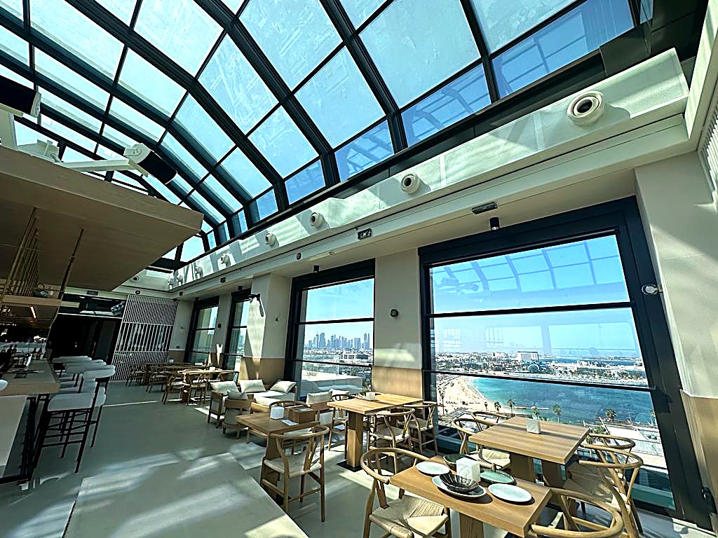 Rooftop dining under a vaulted glass ceiling with floor to ceiling windows onto the sea and skyline