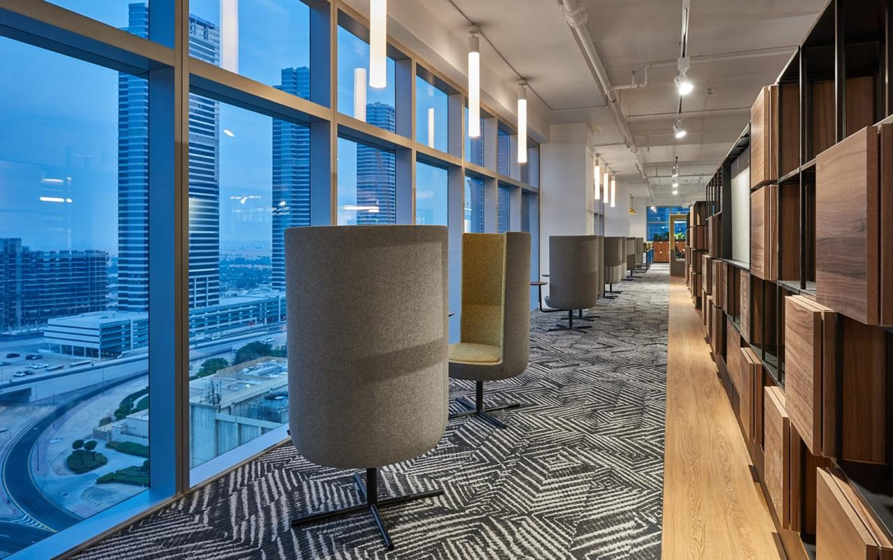 Upholstered high back pod chairs along floor to ceiling glazing with timber storage wall