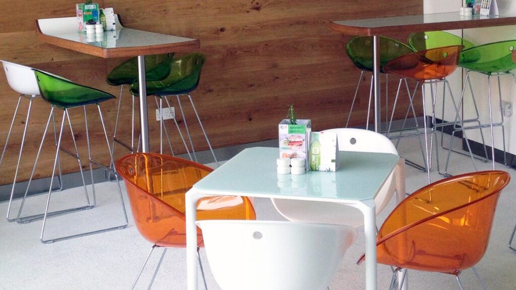 Restaurant seating with orange and green acrylic chairs in front of a timber clad wall