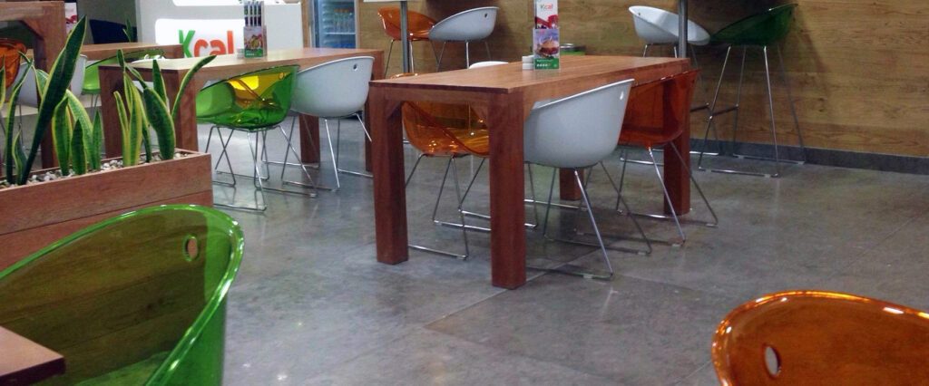 Timber dining tables with acrylic chairs and planters on a polished floor