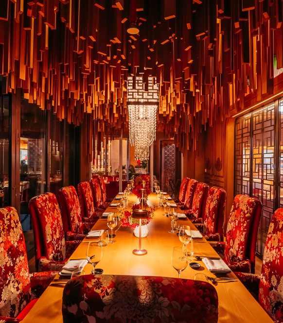 Long private dining table with floral upholstered chairs under a timber baffle ceiling