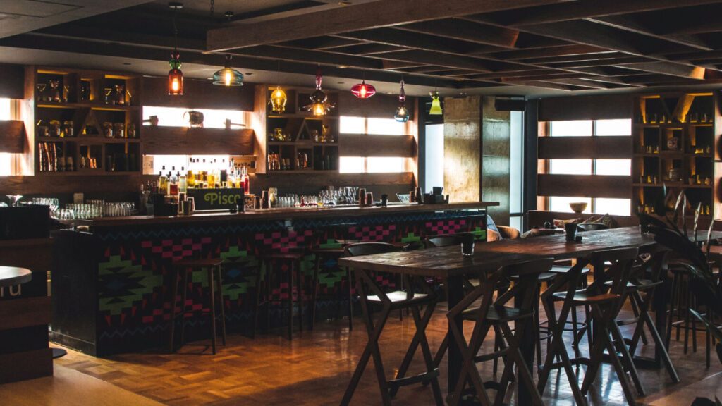 Bar with patterned counter front, high timber tables and backlit shelving