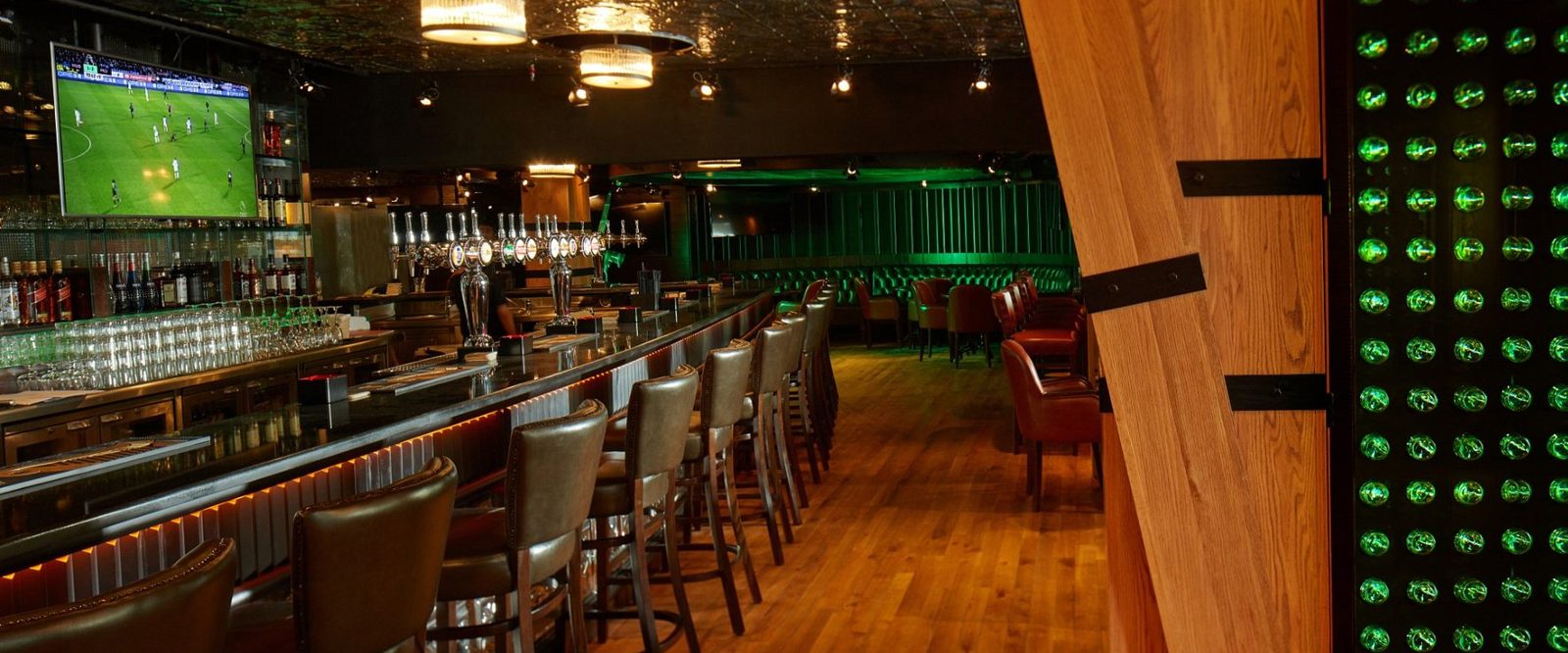 Bar counter with beer taps, sports screens and a green backlit panel