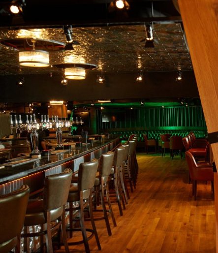 Long bar with leather stools, pressed metal ceiling and green lit booths