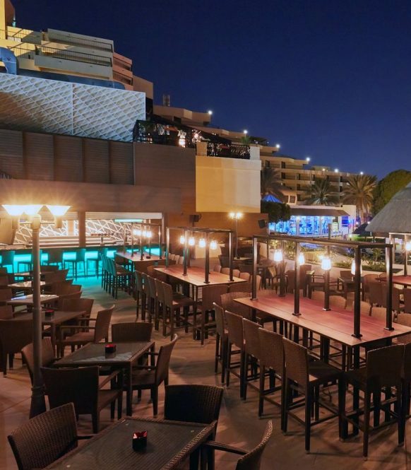 Outdoor terrace at night with lit high tables and a bar counter