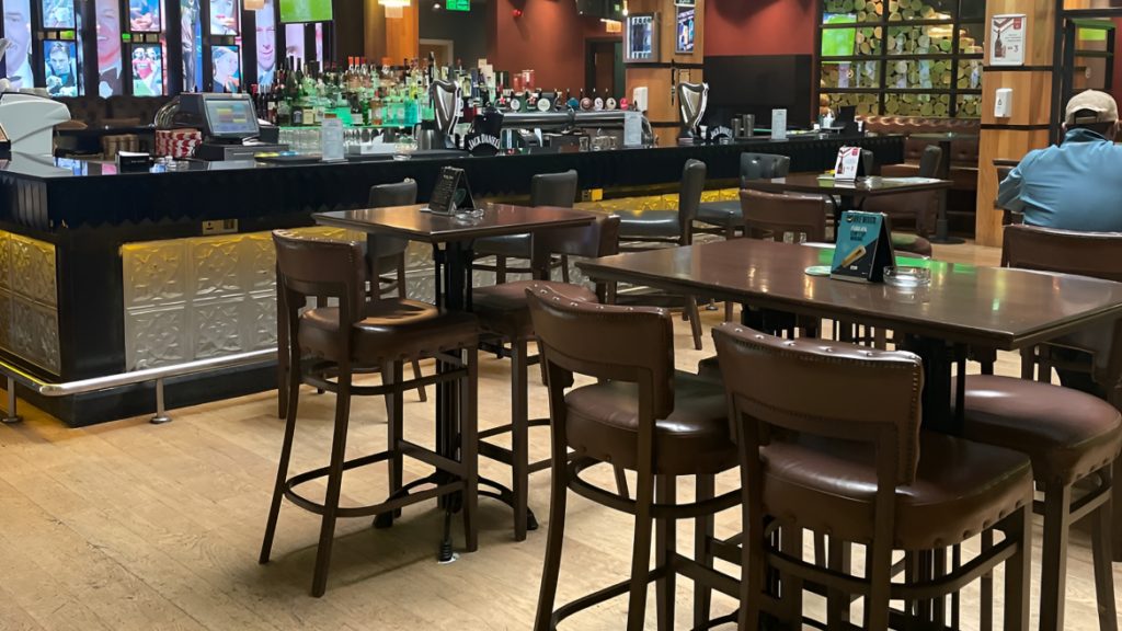Bar counter with high tables and stools and screens above the back bar