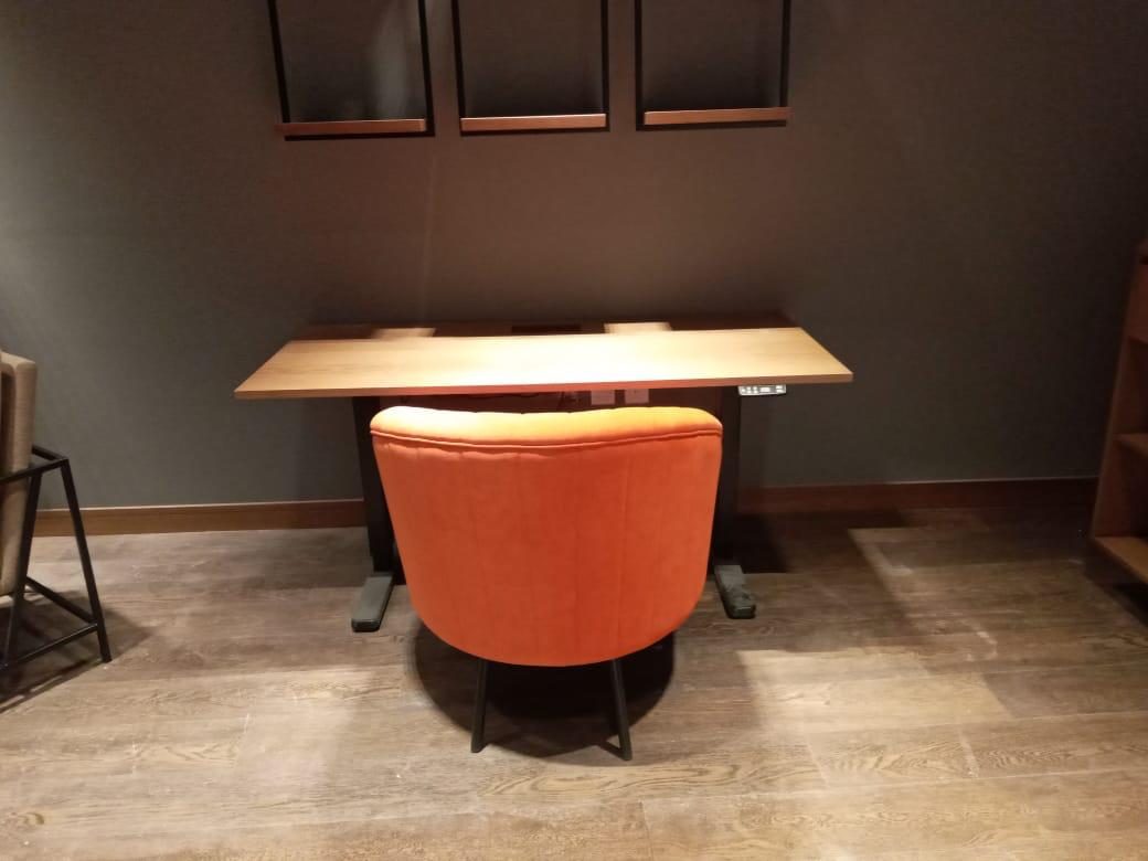 Timber desk with an orange tub chair in a dark walled office, during installation