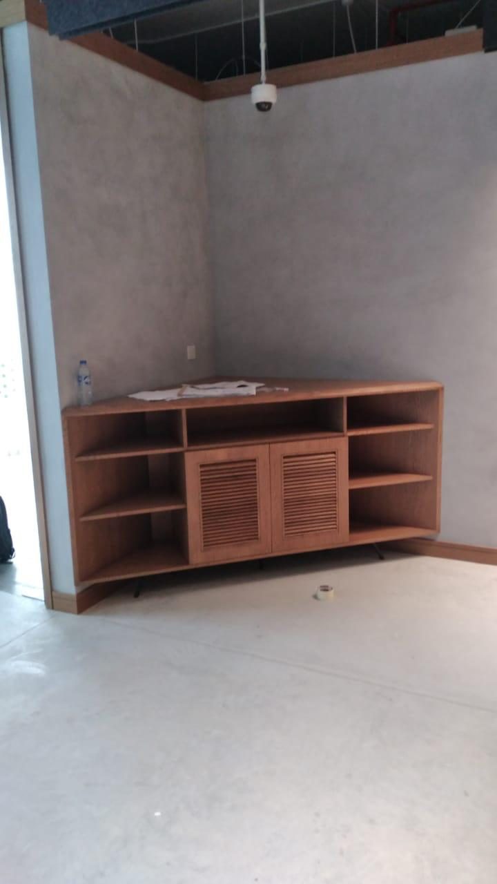 Low timber joinery unit with louvred doors against a concrete wall, during installation
