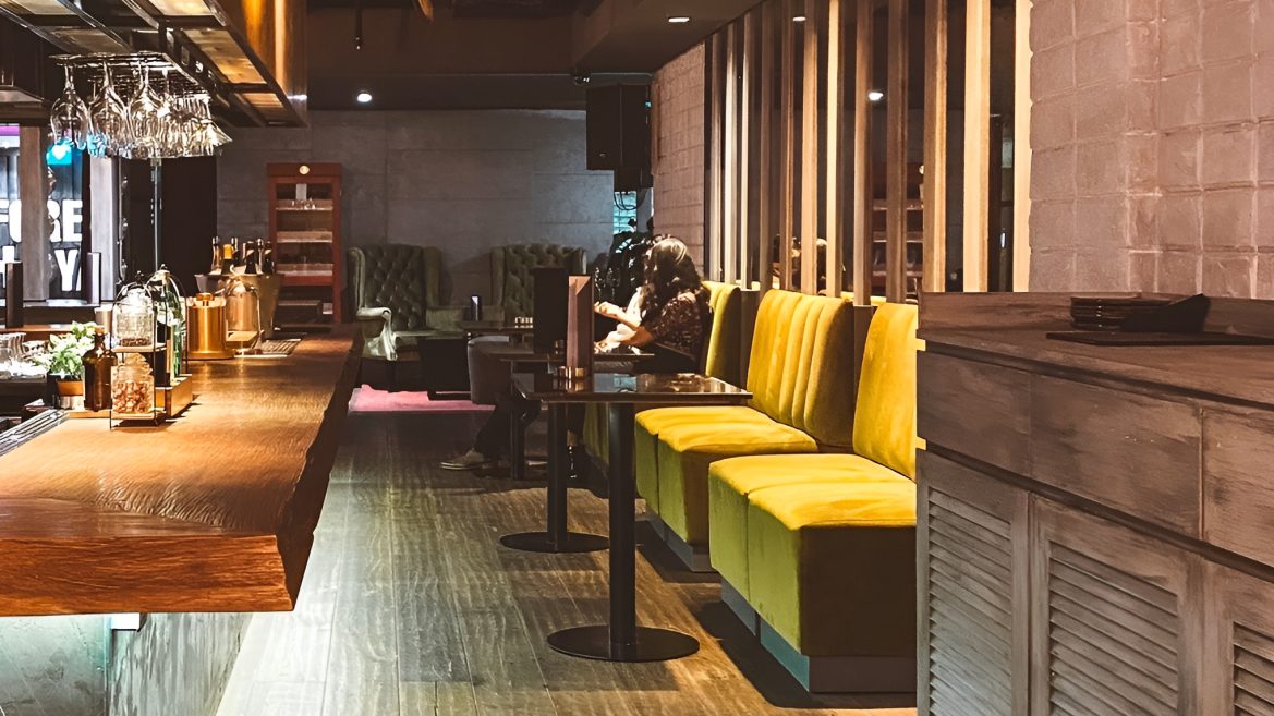 Timber bar counter beside mustard velvet booths and slatted timber screens
