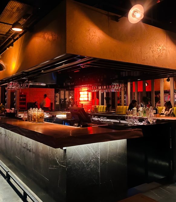 Bar with stone clad counter under a bronze canopy and red neon back bar