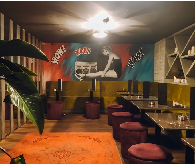 Lounge with pop art mural, olive banquette and burgundy stools