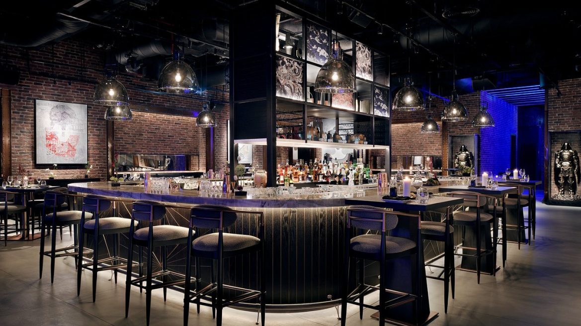 Curved bar with high stools under steel framed shelving and brick walls
