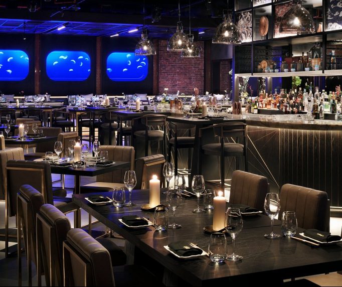 Dining room with leather chairs, candlelit tables and blue lit wall panels