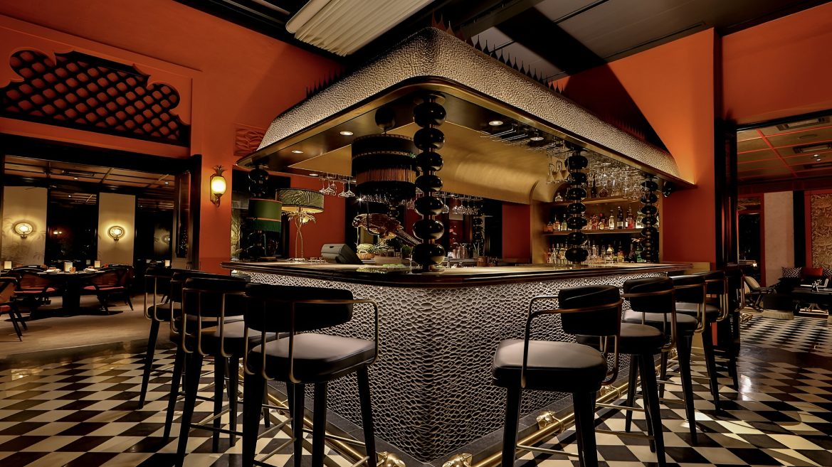 Island bar with patterned front and black stools on a chequered marble floor