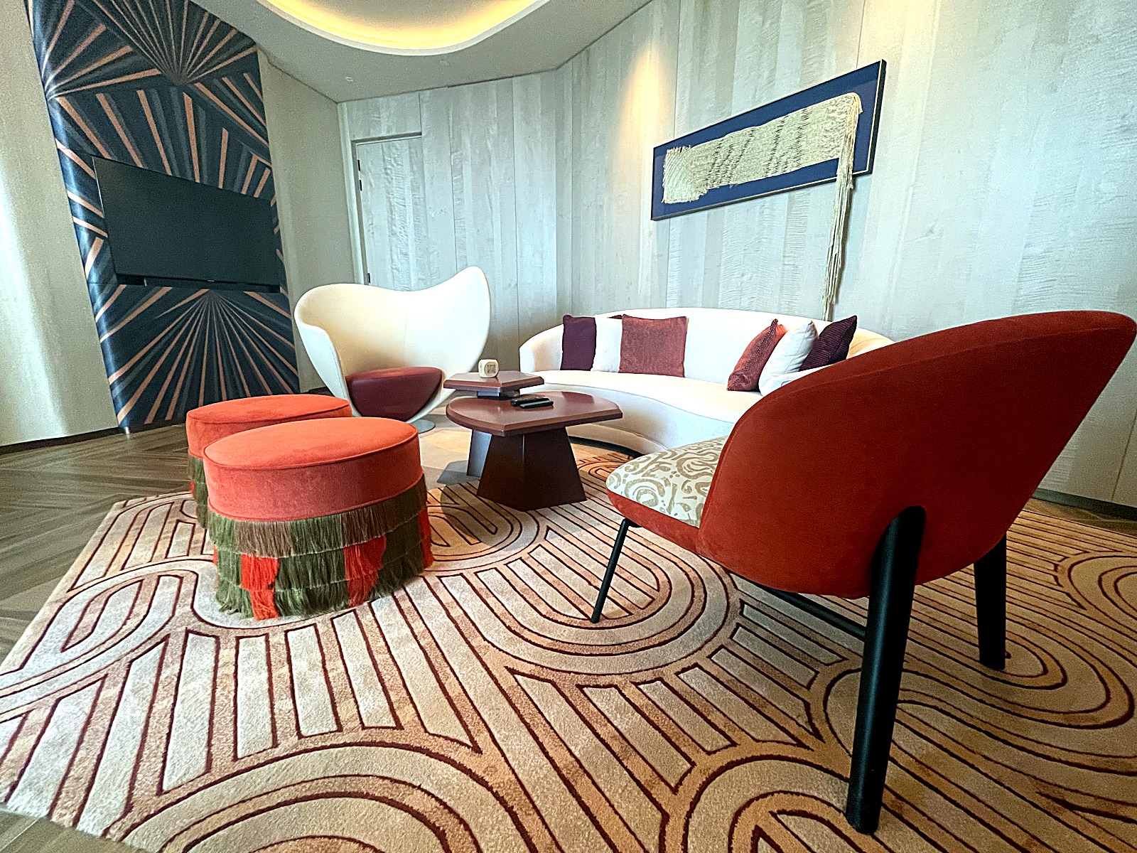 Lounge with red accent chairs and a curved sofa on a graphic patterned rug