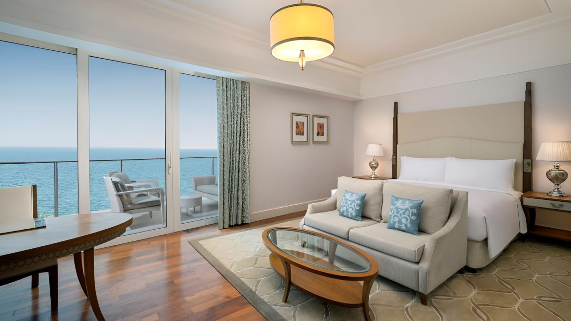 Guest room with four poster bed, sofa and glazed doors to a sea view balcony