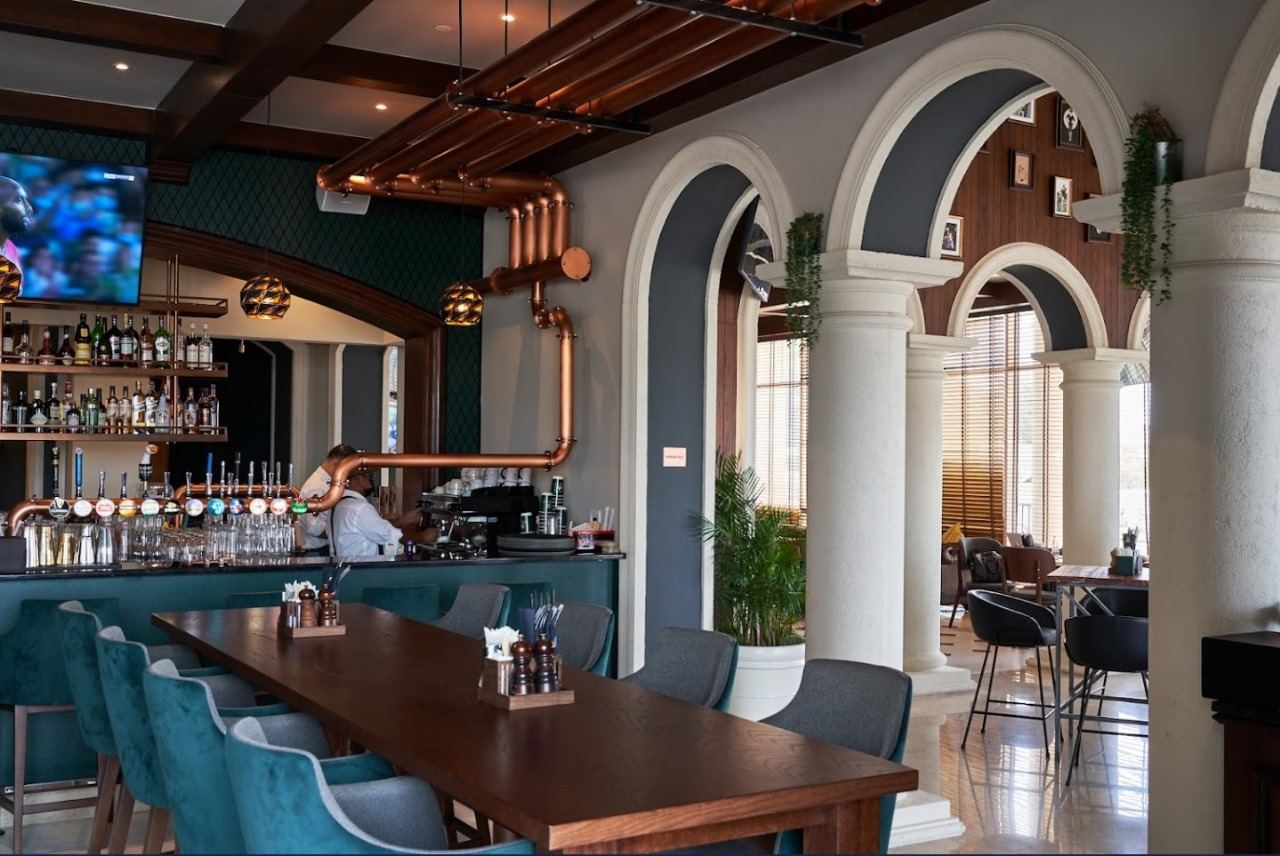 Restaurant bar with arched columns, teal bar stools and a long timber table