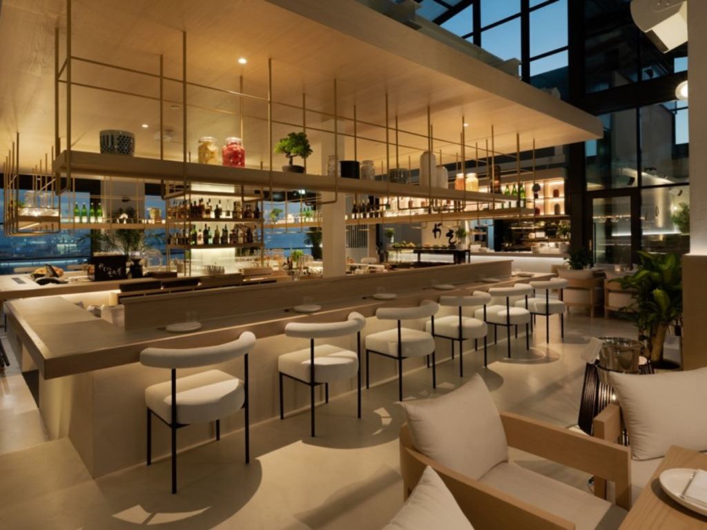 Restaurant bar counter with white stools under a suspended brass shelving frame