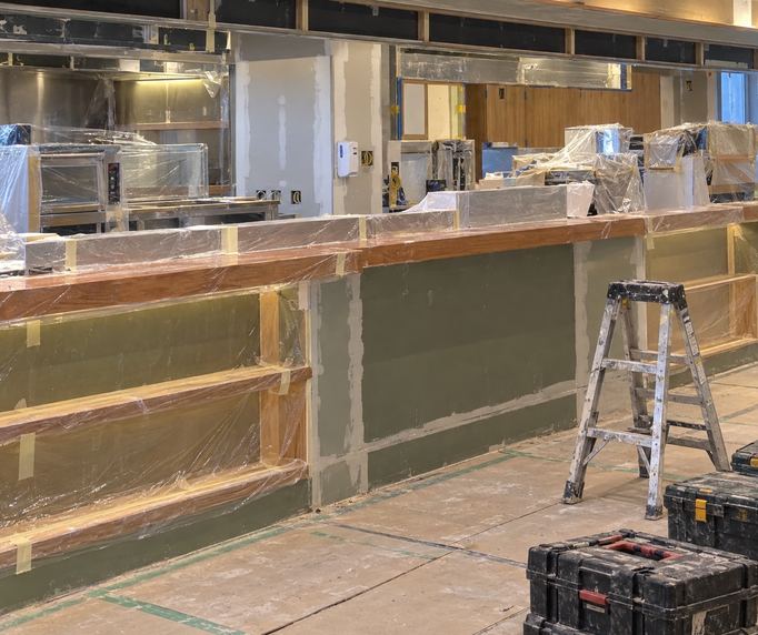 Cafe unit with a timber counter and menu shelving, during fit-out, joinery going in (AI illustration)