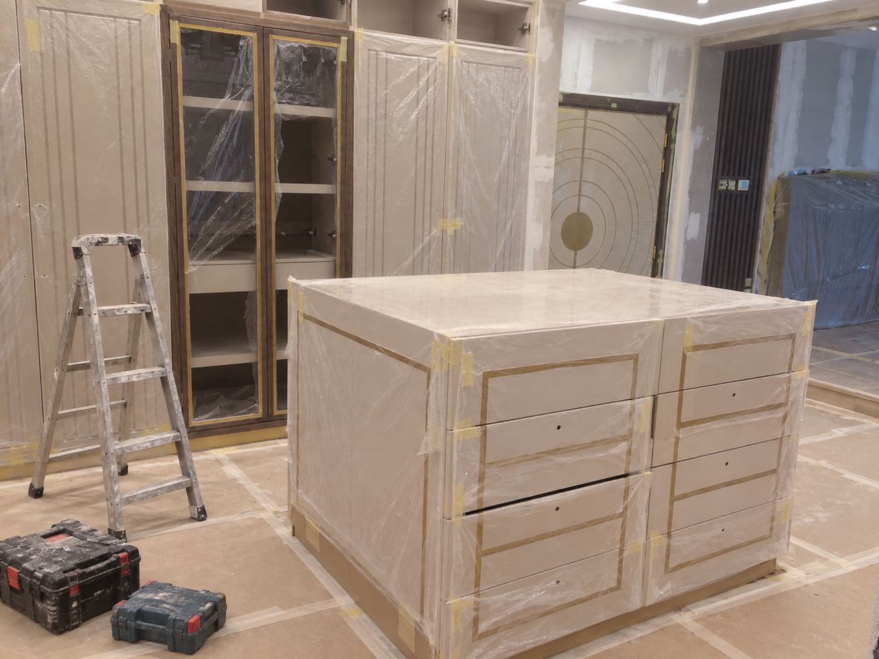 Dressing room with a lacquered island and fitted wardrobes, during fit-out, joinery going in (AI illustration)